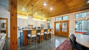 Une cuisine moderne avec un plafond en bois, des armoires blanches et un îlot central doté de tabourets de bar.