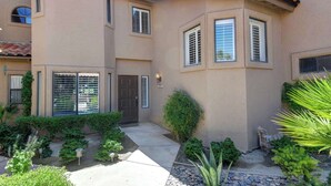 A two-story house with a covered patio, a front door, and a small garden with various plants. - Exclusive 2BR, Golf Views & Private BBQ (Palm Desert)