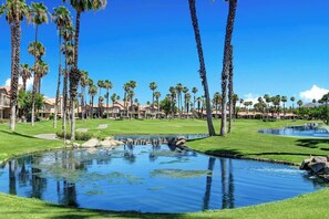 A golf course with a pond, palm trees, and resort buildings. - Exclusive 2BR, Golf Views & Private BBQ (Palm Desert)