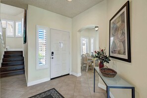 A hallway with a staircase, a door with a security keypad, a dining area with a table and chairs, and a framed artwork on the wall. - Exclusive 2BR, Golf Views & Private BBQ (Palm Desert)