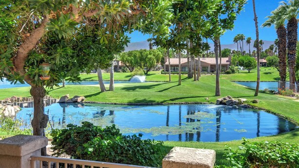 A landscaped area with a pond, palm trees, and a building with a red roof. - Exclusive 2BR, Golf Views & Private BBQ (Palm Desert)