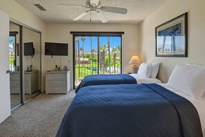 Une chambre d’hôtel avec deux lits, un ventilateur de plafond, une télévision, un bureau avec une lampe et une vue sur un terrain de golf.