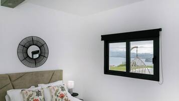 A bedroom with a bed, a circular wall decoration, a window with a view of a lake and mountains, and a nightstand with a lamp.
