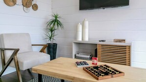 A modern living room with a white sofa, a wooden coffee table, a potted plant, a TV mounted on the wall, and a shelf with decorative items. - GuestReady - Good Vibes | Sea Views, Terrace & BBQ (Ponta Delgada)