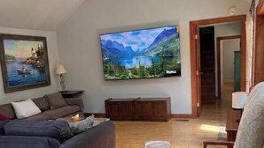 Un salon avec un ventilateur de plafond, un tableau, une grande télévision et un meuble en bois.