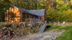 Une cabane avec une façade en bois, des fondations en pierre et un escalier menant à une terrasse.