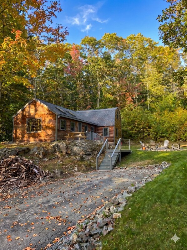 A cabin with a wooden exterior, a stone foundation, and a staircase leading to a deck.