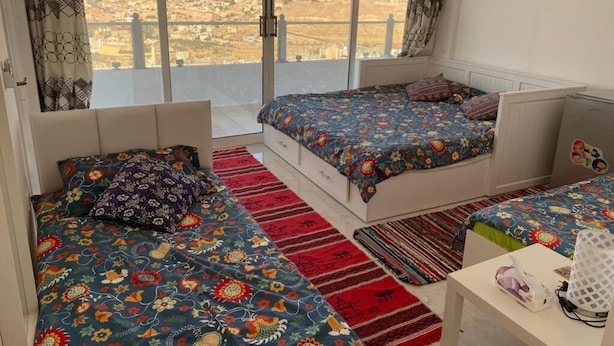 A bedroom with two beds, a view of a town, and a small table with a lamp. - Jordan Guest House (Wadi Musa)