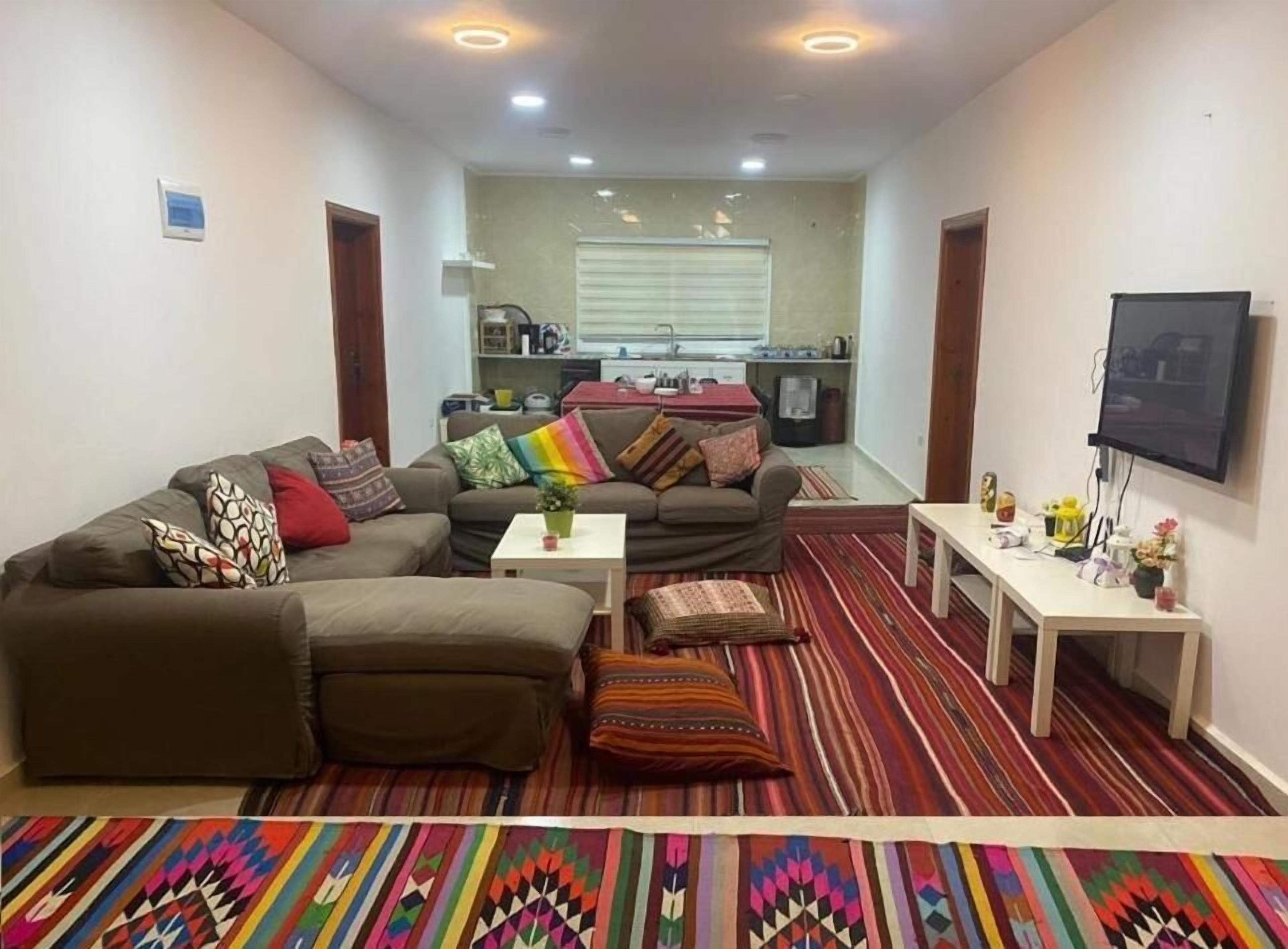 Un salón con un sofá, una mesa de centro y un televisor. Se ve una cocina al fondo.