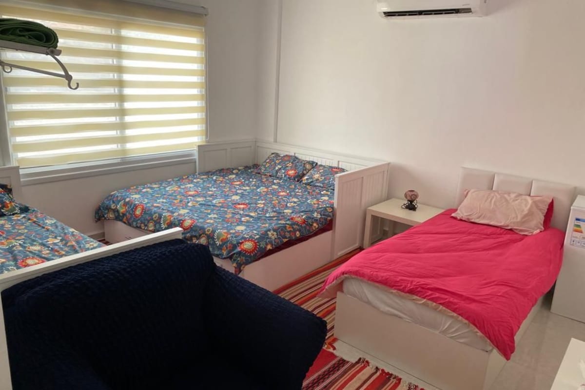 Un dormitorio con dos camas, una silla, una mesita de noche y una ventana con persianas.