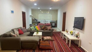 A compact living space with a sofa set, a coffee table, a TV, and a kitchen area in the background. - Jordan Guest House (Wadi Musa)