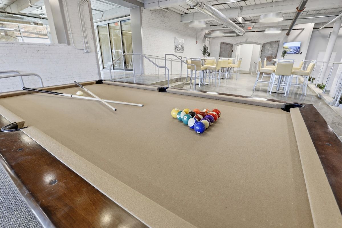 Une table de billard recouverte d’un drap blanc, entourée de chaises et séparée du reste de la pièce par une cloison en verre.