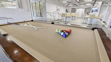 Une table de billard recouverte d’un drap blanc, entourée de chaises et séparée du reste de la pièce par une cloison en verre.