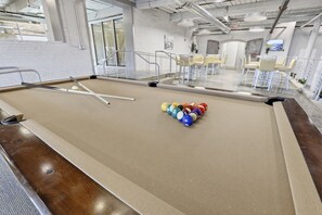 A pool table with a white cloth, surrounded by chairs and a glass partition.