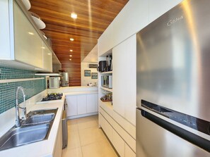 A modern kitchen with a stainless steel refrigerator, white cabinets, and a wooden ceiling. - Bangalo com Piscina Privativa no Malawi Beach Porto de Galinhas (Ipojuca)