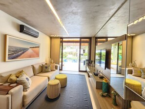 A modern living room with a sofa, ottomans, a coffee table, a large mirror, and a painting of a beach scene. - Bangalo com Piscina Privativa no Malawi Beach Porto de Galinhas (Ipojuca)