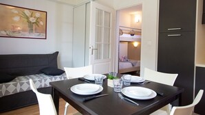 Een kleine kamer met een eettafel gedekt voor twee personen, een bank, een stapelbed en een donkere garderobe.