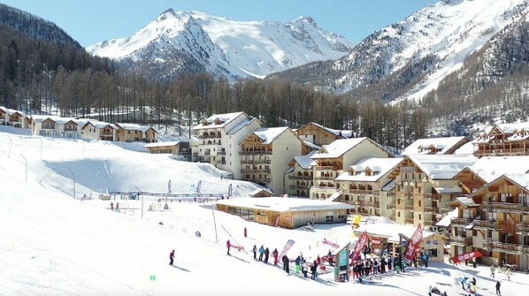 Une station de ski avec des bâtiments de style chalet, une piste de ski et un paysage montagneux en toile de fond.