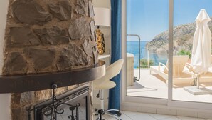 Un mur de pierre, une chaise blanche, une vue sur la mer et un balcon avec un parasol blanc.