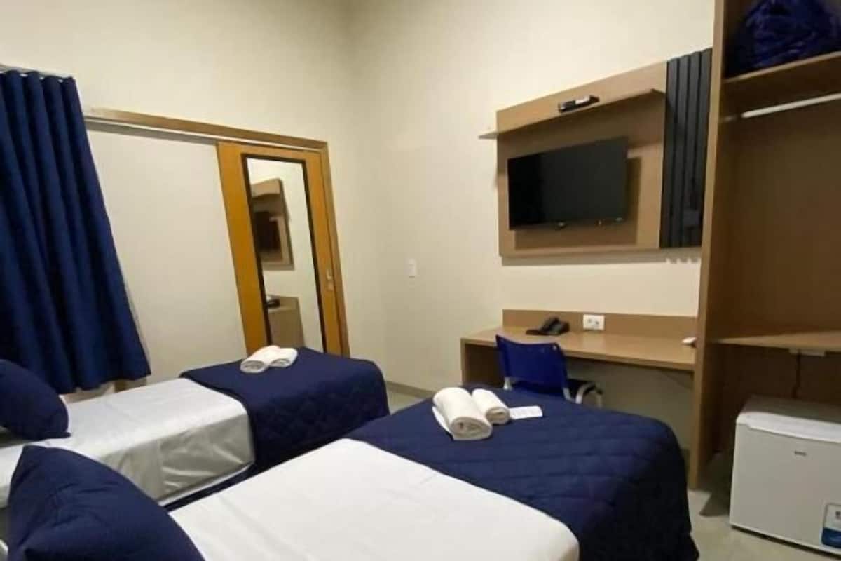 A hotel room with two beds, a desk, a television, and a refrigerator.