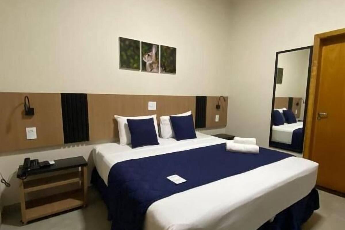 A hotel room with a large bed, a bedside table, a mirror, and a door.