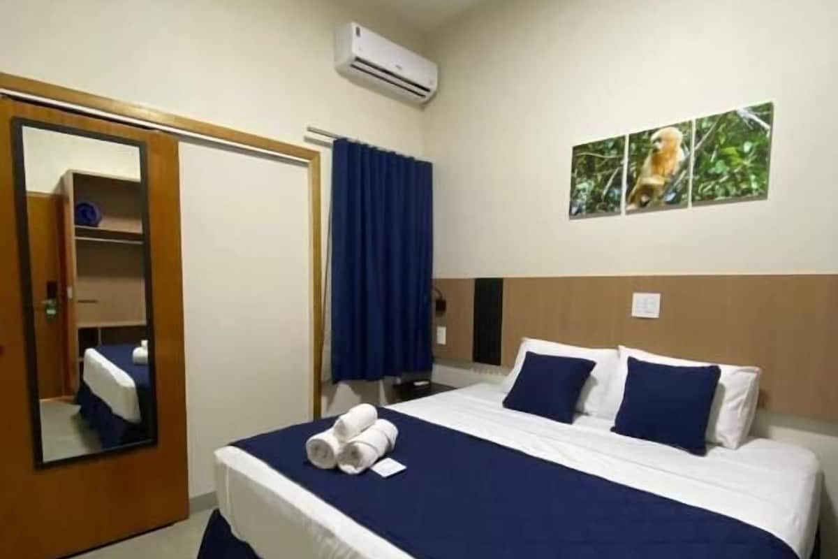 A hotel room with a large bed, a wardrobe, a mirror, and an air conditioning unit.