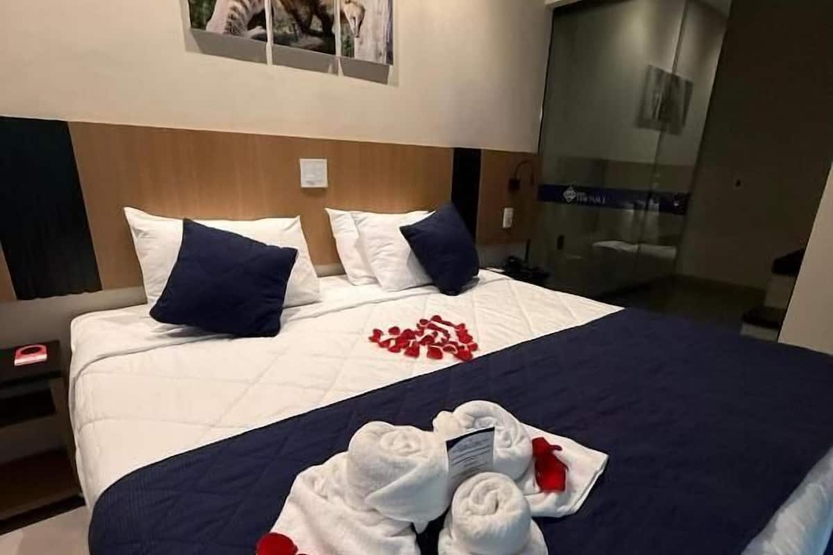 A modern hotel room with a large bed, a wooden headboard, and a glass door leading to a balcony.