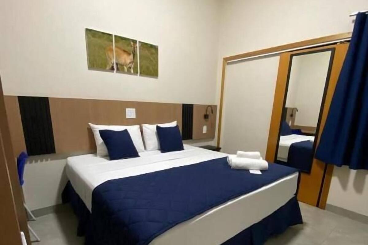 A hotel room with a large bed, a mirror, and a picture on the wall.