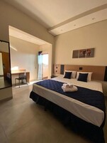 A hotel room with a large bed, a desk, and a view of the outside.