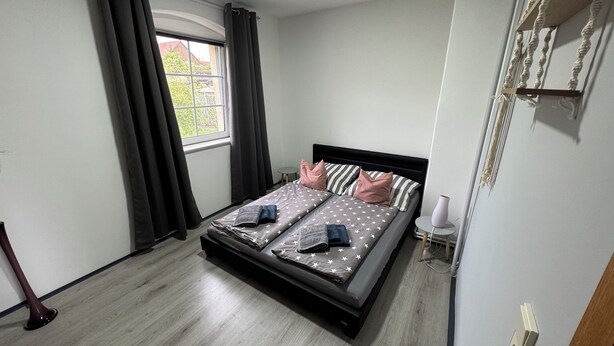Une chambre à coucher avec un lit, des rideaux, une fenêtre et une table de chevet avec une lampe.