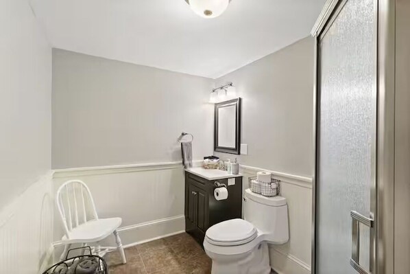 A bathroom with a white toilet, a black vanity with a mirror, and a white chair.