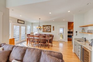 A spacious living room with a brown leather couch, a dining area with wooden chairs and a table, a kitchen with stainless steel appliances, and a large window providing natural light. - 5 Bedroom/5 Bathroom Single Family Home at Coolidge Falls. Concierge Services Available (Lincoln)