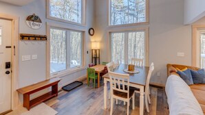 A cozy room with a wooden bench, a dining table with chairs, and large windows offering a view of trees. - Waterville Estates- Tons of Amenities! (Campton)