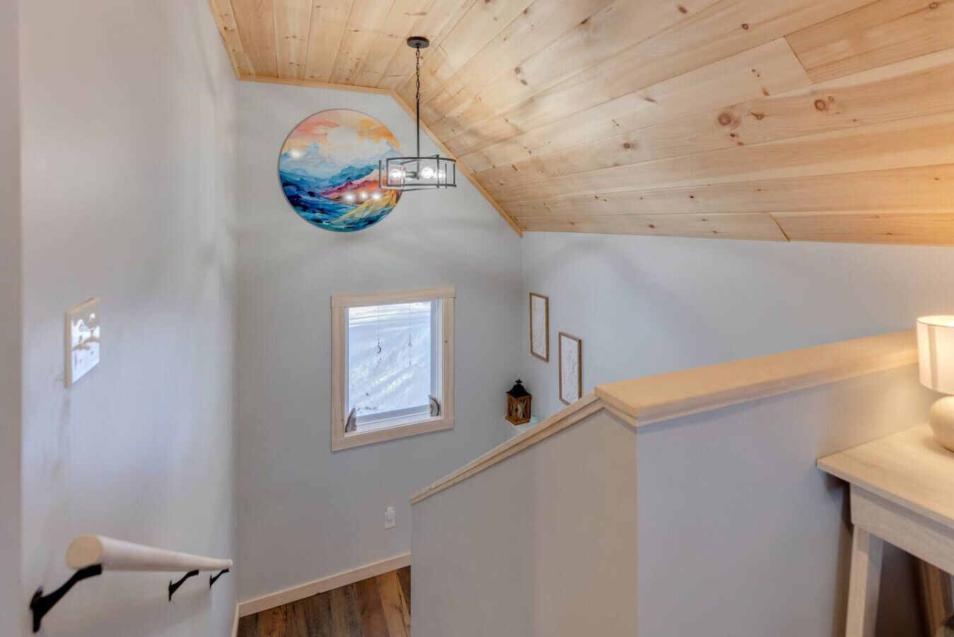 A staircase with a wooden ceiling, a wall-mounted globe, a small window, and a wall-mounted light fixture.