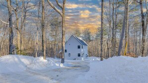 A white house with a gabled roof surrounded by a snowy landscape and leafless trees. - Waterville Estates- Tons of Amenities! (Campton)