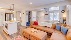 A modern living room with a large sofa, a coffee table, and a kitchen area with a refrigerator and island. - Waterville Estates- Tons of Amenities! (Campton)