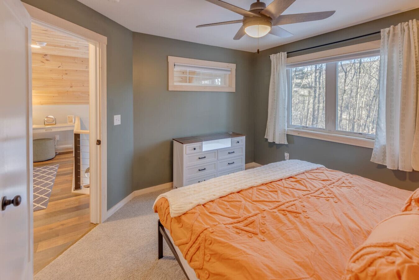 A bedroom with a bed, a dresser, a ceiling fan, and a window with curtains.