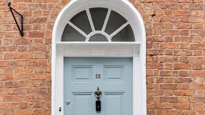 Una puerta azul claro con un arco blanco, el número 12 encima y un buzón pequeño debajo.
