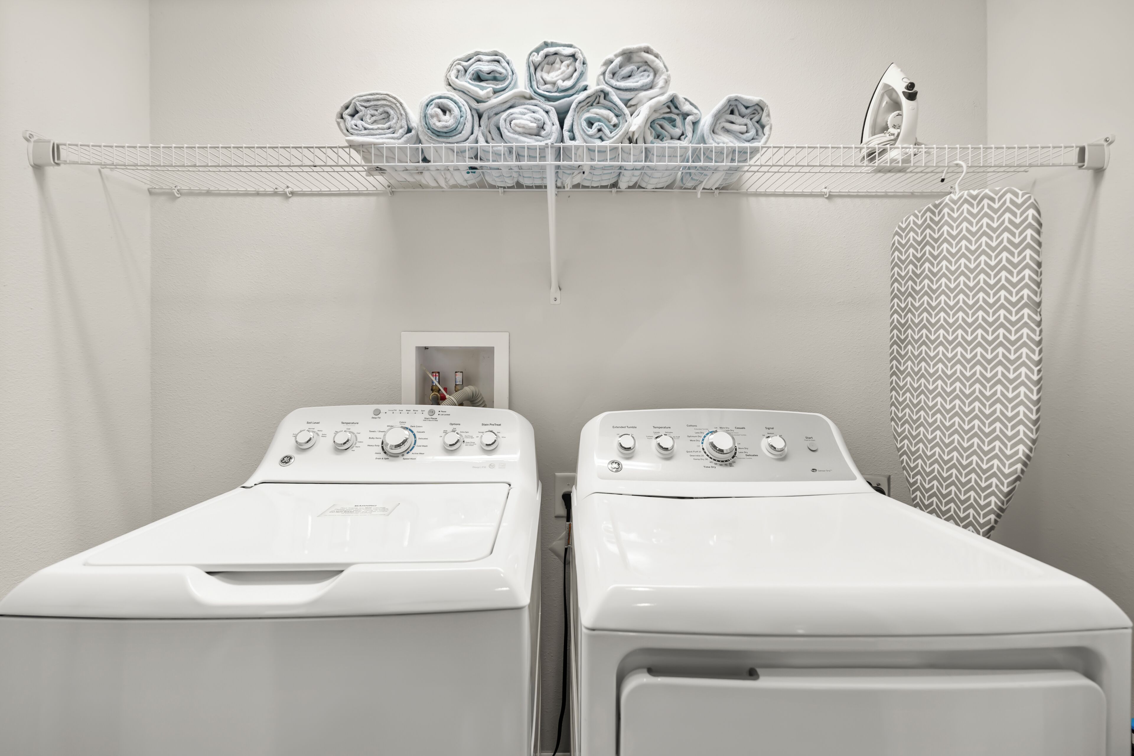 Un espace buanderie comprenant deux machines à laver à chargement frontal, un étendoir avec des serviettes pliées et un rideau de douche suspendu.