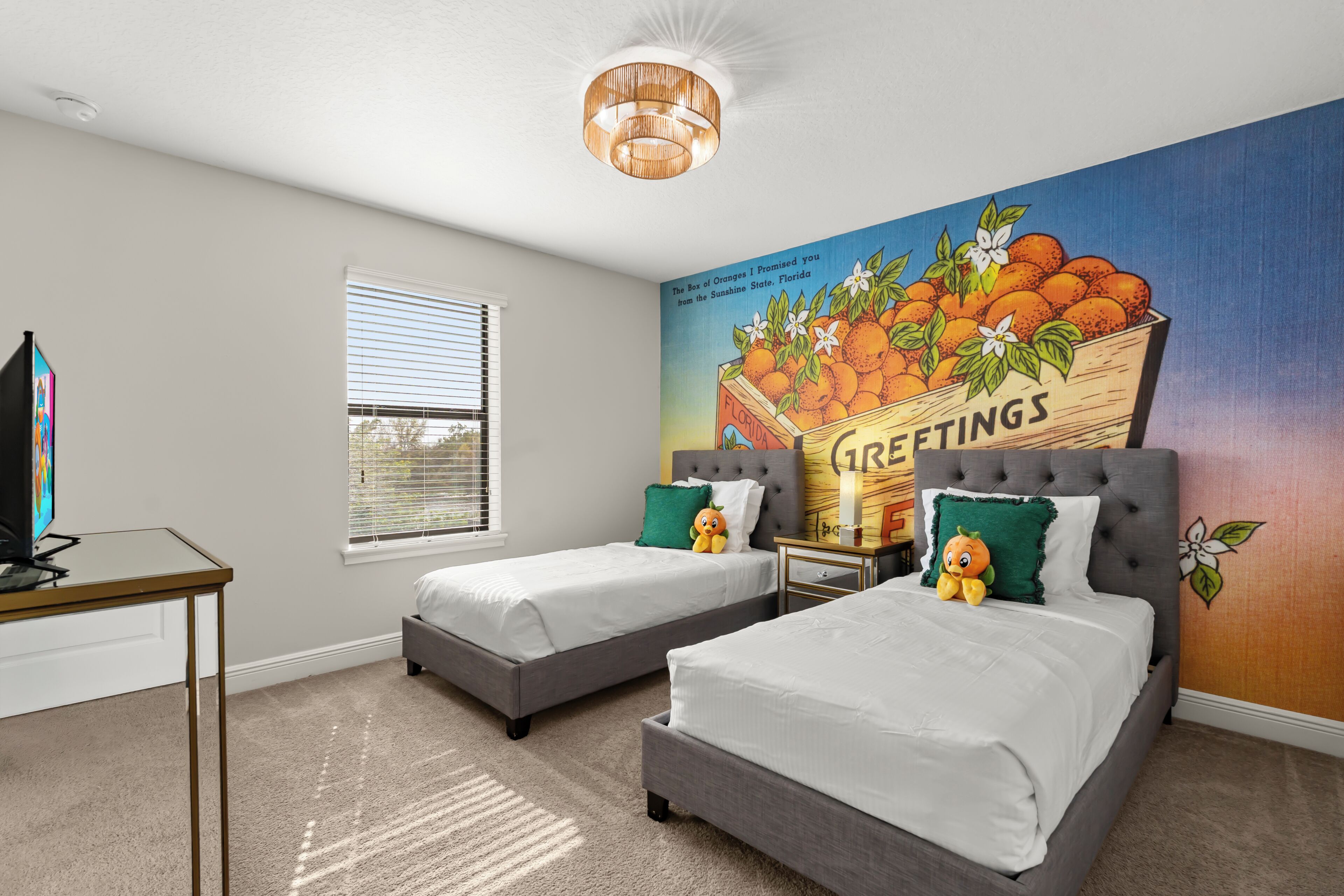 A bedroom with two beds, a TV, and a mural of oranges on the wall.