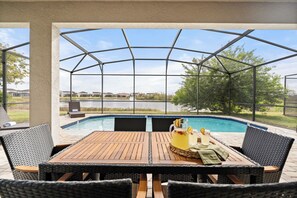 A covered patio with a pool, wicker furniture, and a table with a pitcher of lemonade. - Citrus Grove Getaway in the Heart of Florida (Haines City)
