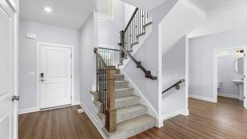 A staircase with wooden steps and metal railings, leading to a landing with a white door and a light switch on the wall.