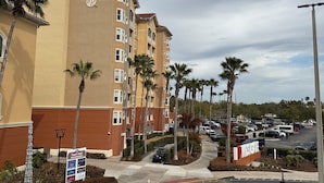 Ein mehrstöckiges Hotel mit sandfarbener Fassade, Palmen und einem Parkplatz mit Autos.