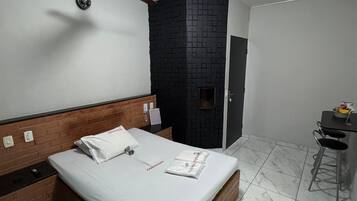 A modern hotel room with a wooden headboard, a bed with white linens, a black accent wall, a ceiling fan, and a small desk with a chair.