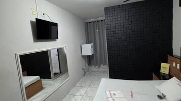Ein modernes Hotelzimmer mit einem Bett, einem an der Wand montierten Fernseher, einem Deckenventilator und einem Vorhangfenster.