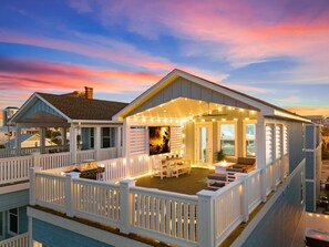A waterfront house with a covered deck, outdoor seating, and string lights. - Deja Blue (Panama City Beach)