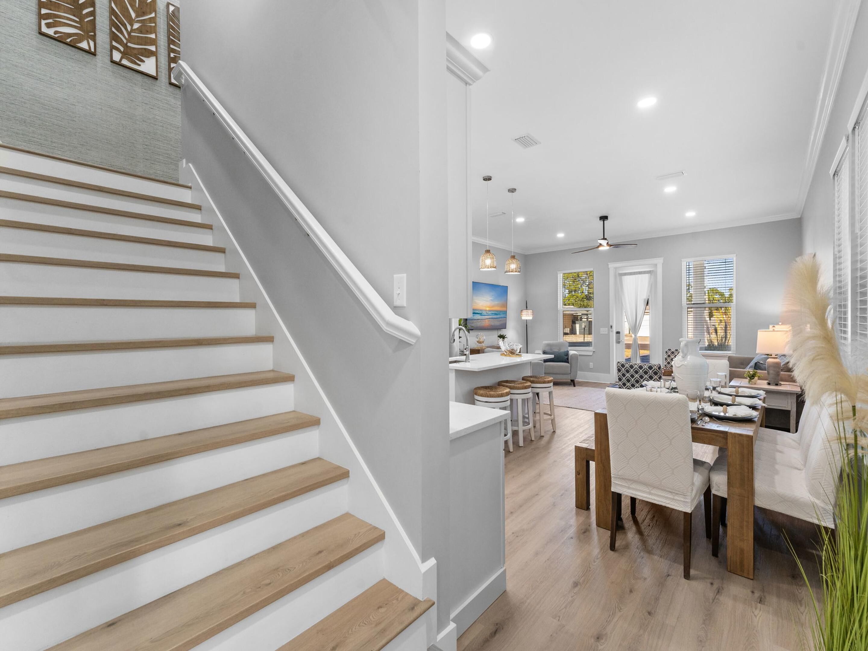 A modern kitchen with a central island, a dining area with a wooden table and chairs, and a staircase with wooden steps.