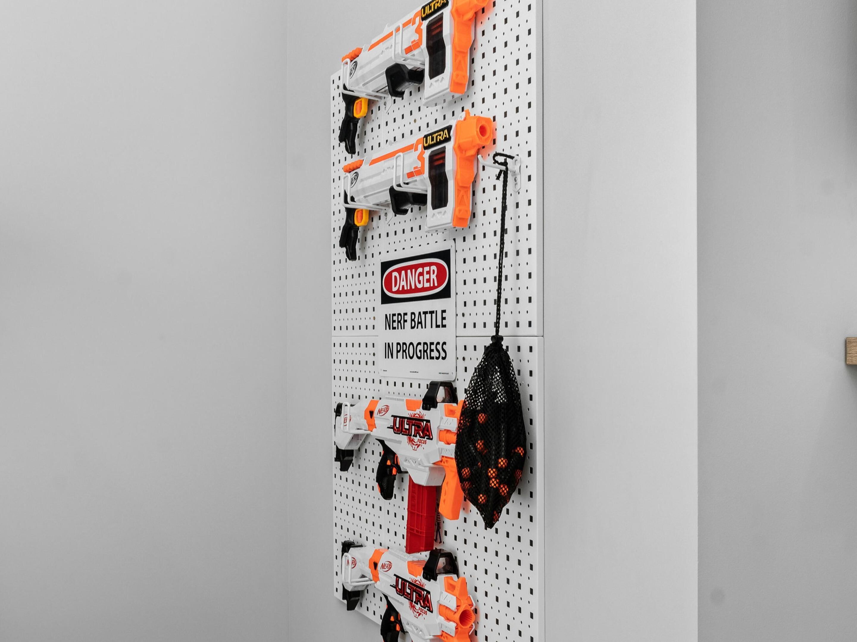 A pegboard with various Nerf blasters and a warning sign.