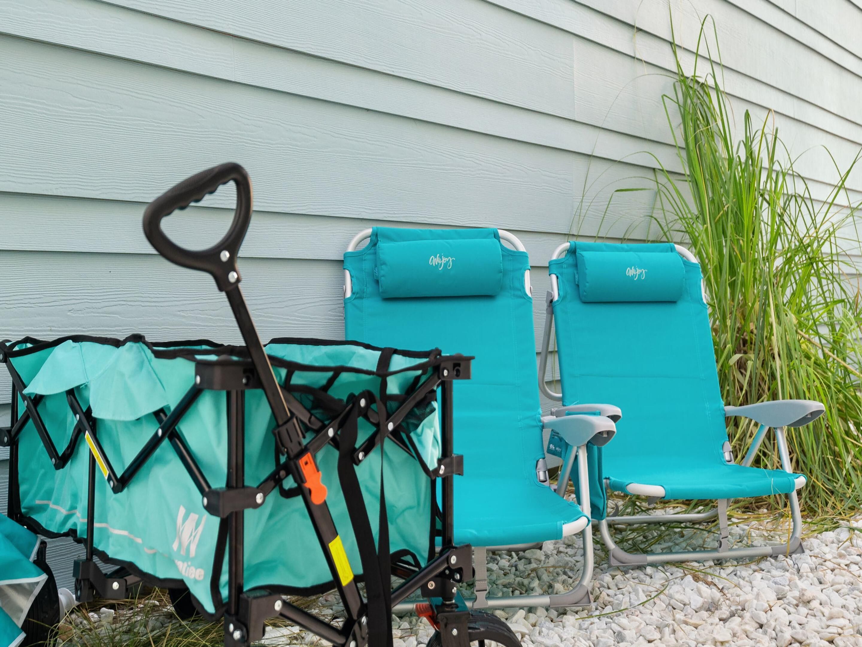 A teal beach chair and a stroller with a matching cover, both placed on a gravel surface in front of a light blue house.