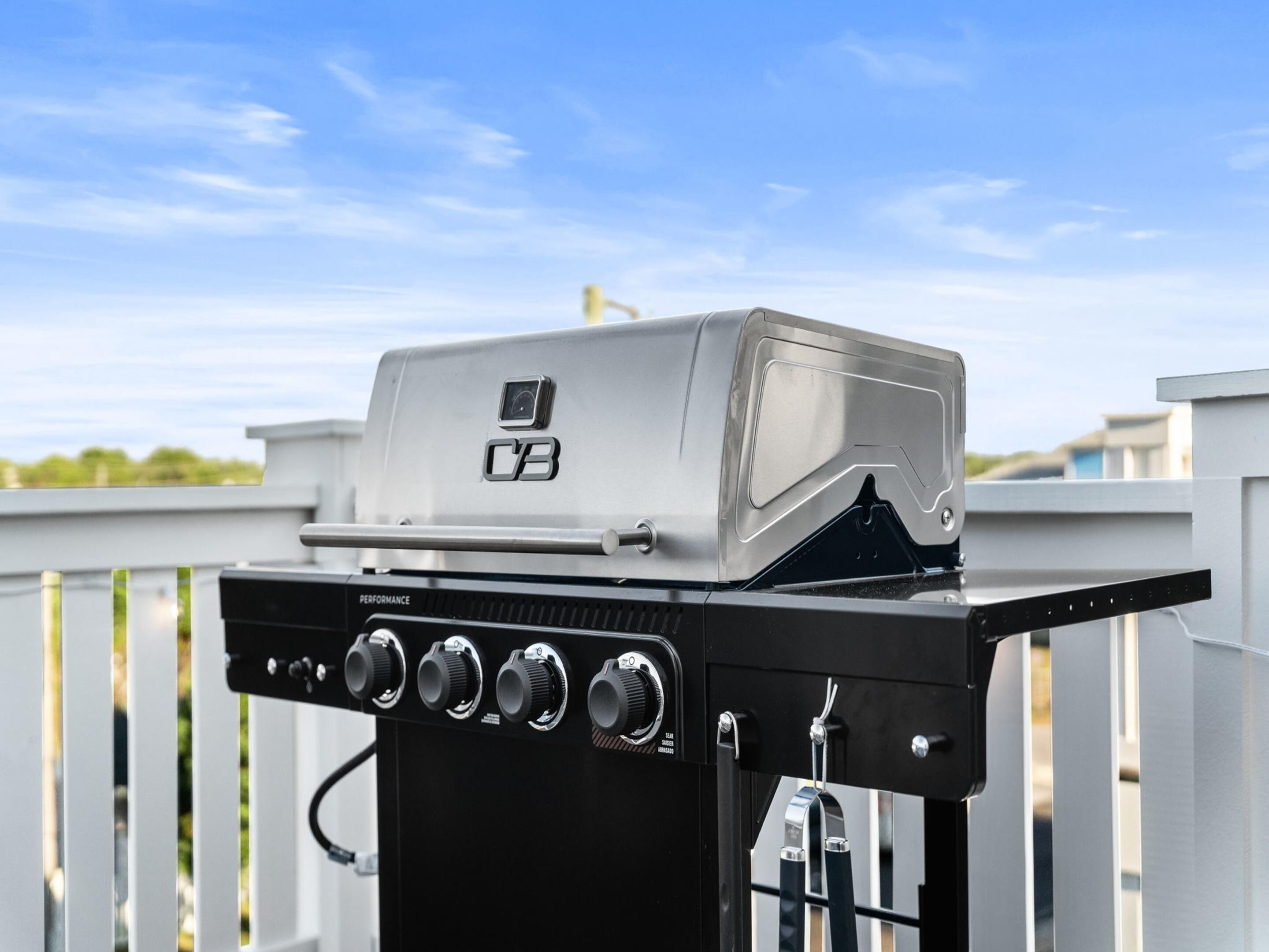 Ein tragbarer Grill mit digitaler Anzeige und mehreren Bedienelementen vor einem weißen Zaun und blauem Himmel.